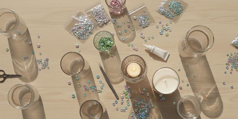 Glass candle holders, pastel rhinestones, glue, and tools for a DIY candleholder project