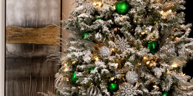 Sapin de Noël blanc floqué orné de boules en verre vert émeraude, de boules argentées et de lumières chaudes créant une ambiance de fête magique