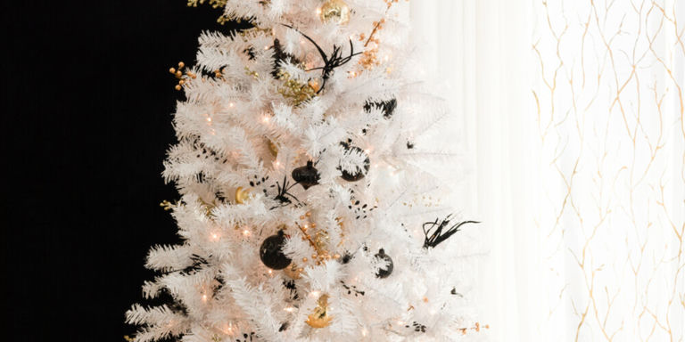 Sapin de Noël blanc floqué, élégant, décoré de boules dorées, de guirlandes de perles et de lumières chaudes scintillantes sur fond noir