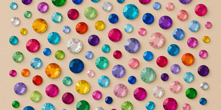 Colorful array of faceted rhinestone gems in rainbow colors including pink, blue, green, purple, and gold scattered on beige background