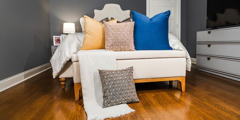 Chambre avec superposition de coussins décoratifs pêche, or rose perlé et bleu sur lit blanc
