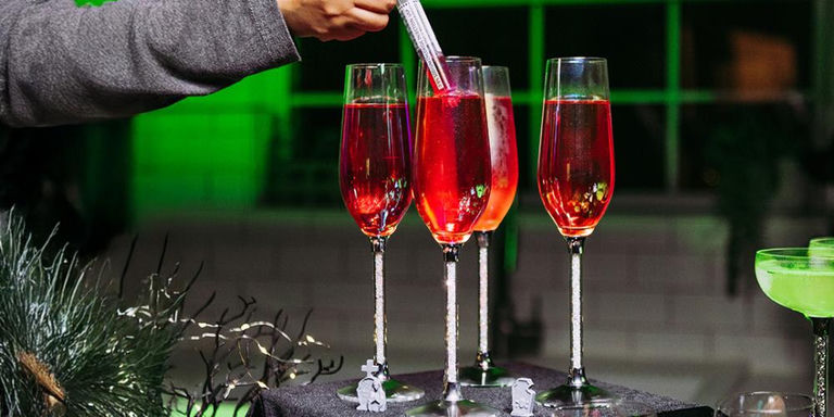 Trois verres à pied remplis de cristaux avec cocktails rouges et seringue en garniture sur une table d’Halloween sombre
