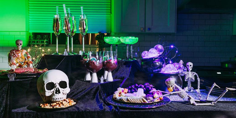 Table de fête d’Halloween effrayante avec décorations de squelette, verres en cristal, cocktails et effets de lumière violette
