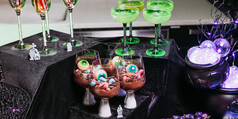 Table de desserts d’Halloween avec verres à pied en cristal, cocktails verts, mousse au chocolat avec yeux comestibles et décorations effrayantes