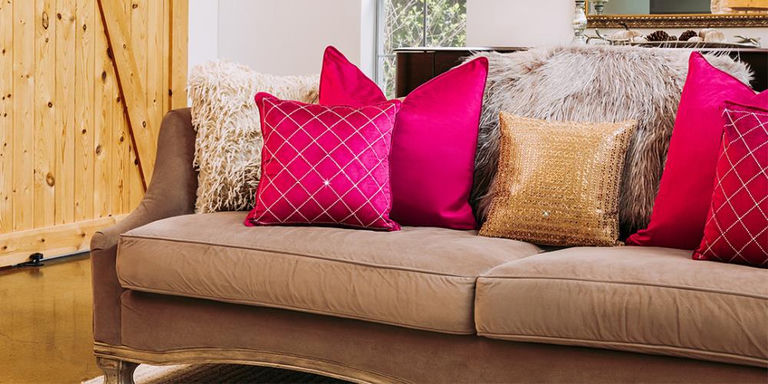 Superposition de coussins décoratifs avec perles dorées, velours rouge et motifs sur un canapé taupe