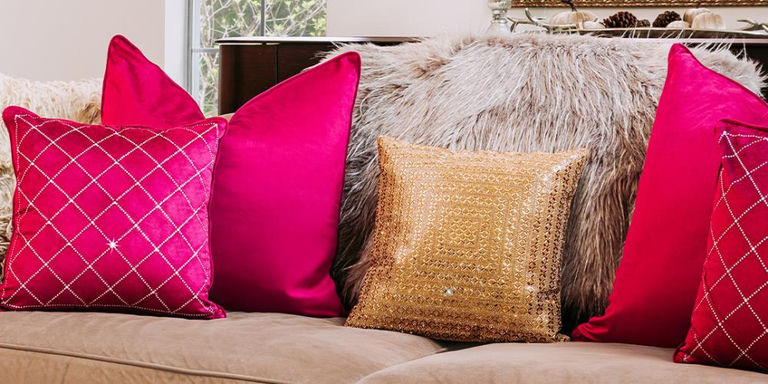 Coussin perlé doré superposé avec des coussins en velours rouge et à motifs sur un canapé neutre