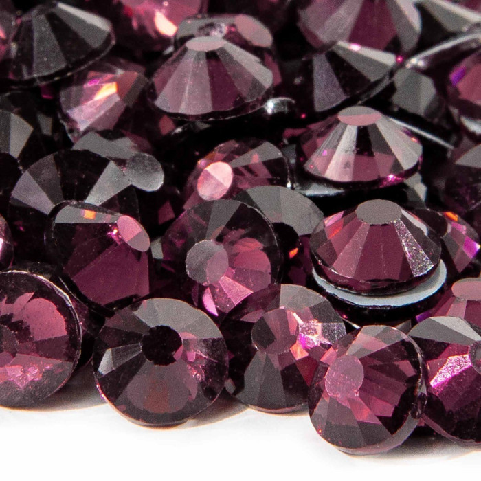 Machine cut crystal rhinestones in deep amethyst with faceted surfaces and gray glue backing varying in size and sparkle.