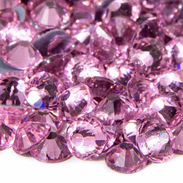 Machine cut crystal rhinestones in light rose faceted with a smooth surface and gray glue backing scattered on a white background.
