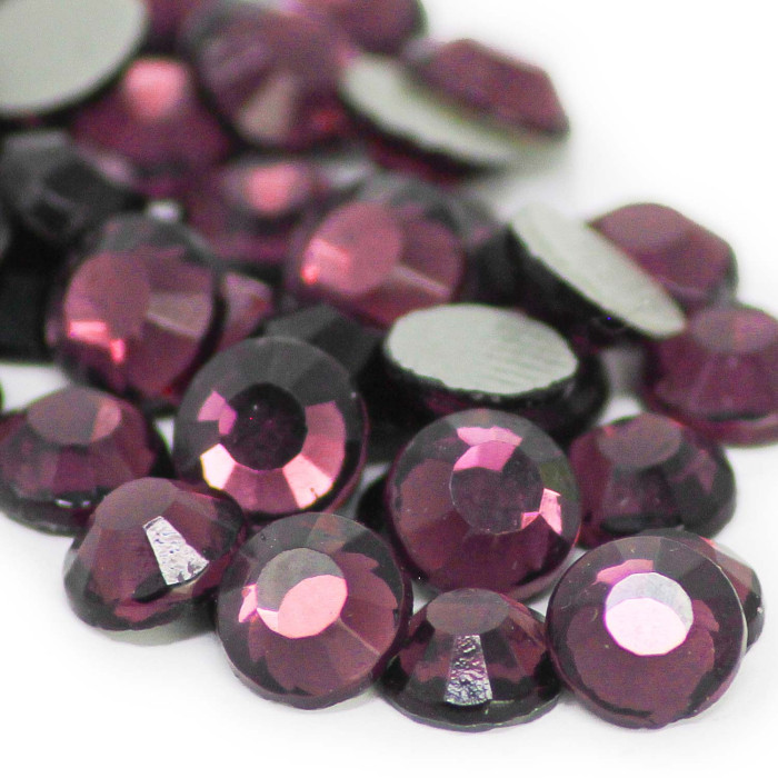 Faceted round amethyst imitation stones in deep purple with a glossy finish and flat black backing varying sizes scattered together.