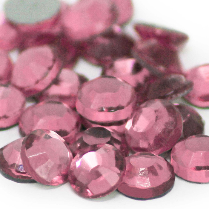 A pile of round faceted light rose glass stones with a glossy finish and a strong black glue backing.
