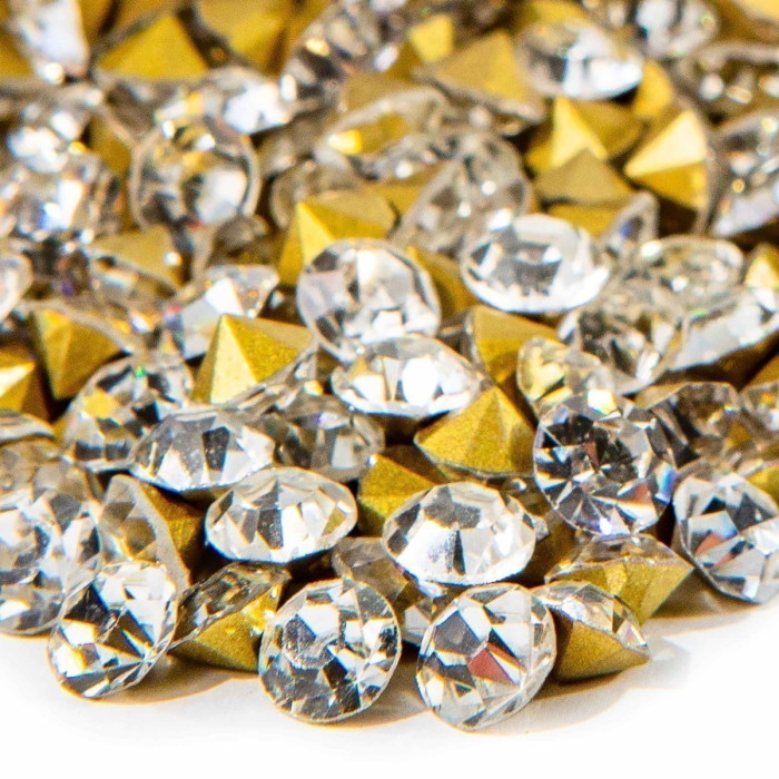 Clear faceted rhinestones and gold pointback cones scattered together on a white surface.