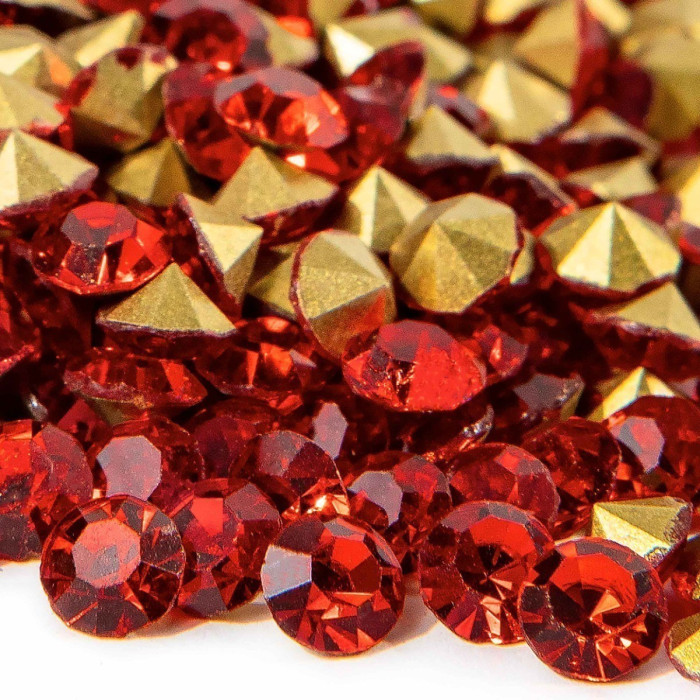 Red faceted round rhinestones and gold pointed-back stones scattered together showcasing a shiny surface and varied sizes.
