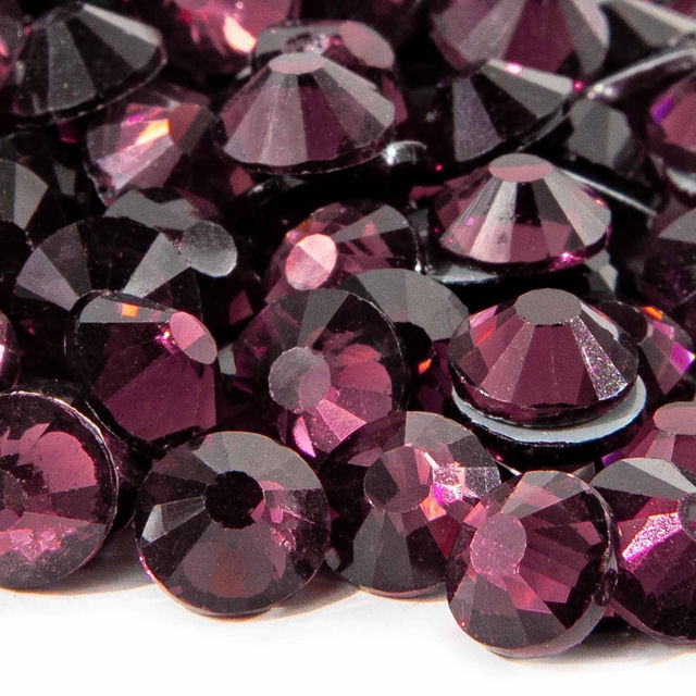 Machine cut crystal rhinestones in deep amethyst with faceted surfaces and gray glue backing varying in size and sparkle.