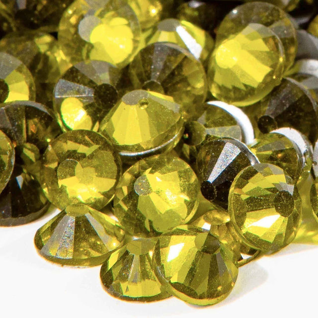 Machine cut crystal rhinestones in vibrant lime green with faceted surfaces and gray glue backing various sizes and shapes.