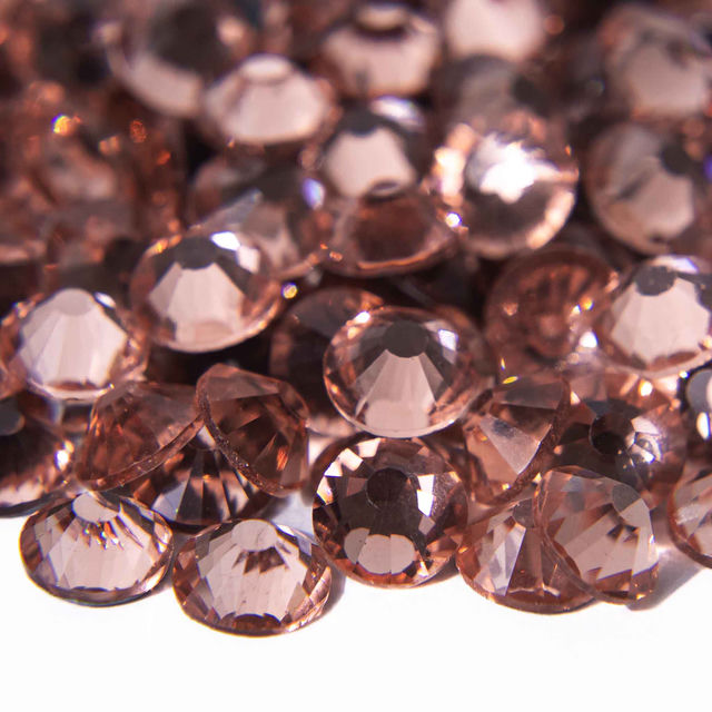 Machine cut crystal rhinestones in peach with faceted surfaces and gray glue backing varying in size and slight color differences.