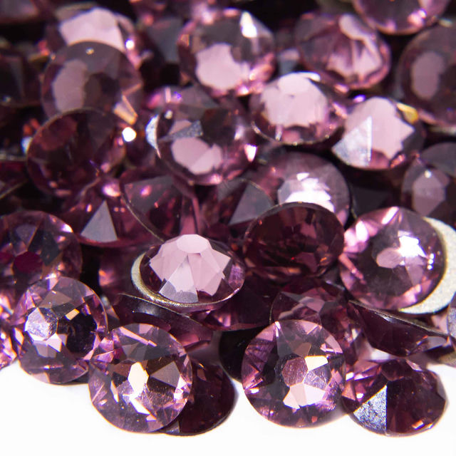 A pile of light amethyst flatback rhinestones with 14 facets exhibiting a shiny smooth surface and varying shades of purple.