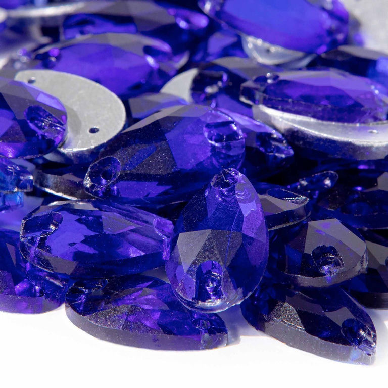 Cobalt teardrop-shaped rhinestones with faceted surfaces and small sewing holes featuring deep blue and purple hues.