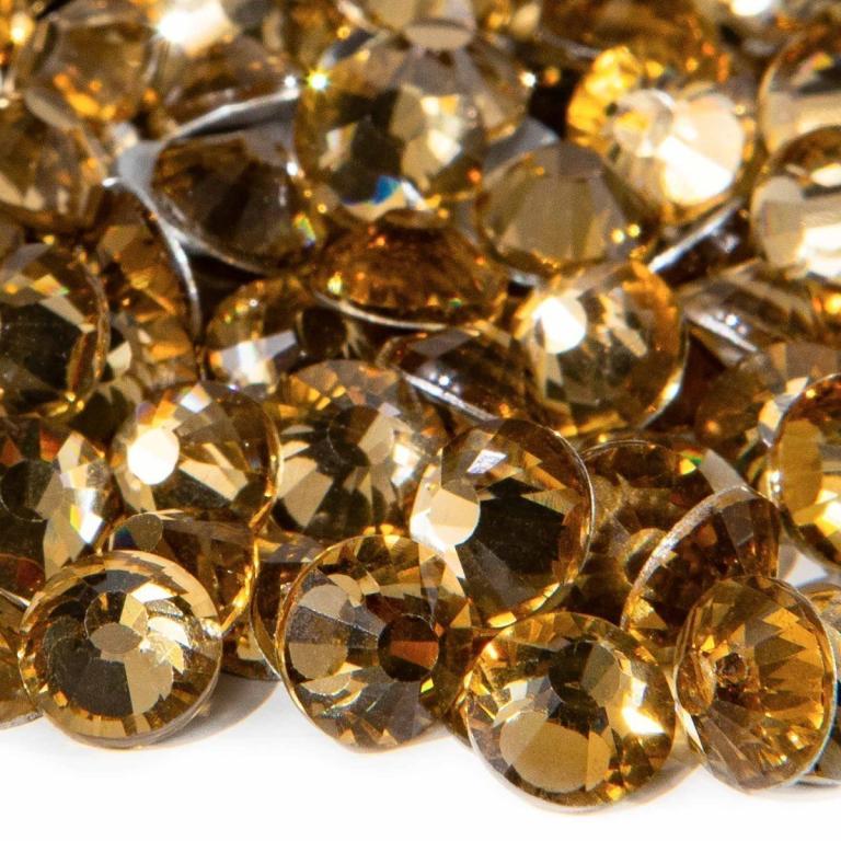 A&#x20;pile&#x20;of&#x20;round&#x20;flatback&#x20;rhinestones&#x20;in&#x20;light&#x20;amber&#x20;with&#x20;12-16&#x20;facets&#x20;and&#x20;silver&#x20;metal&#x20;backing&#x20;reflecting&#x20;light.