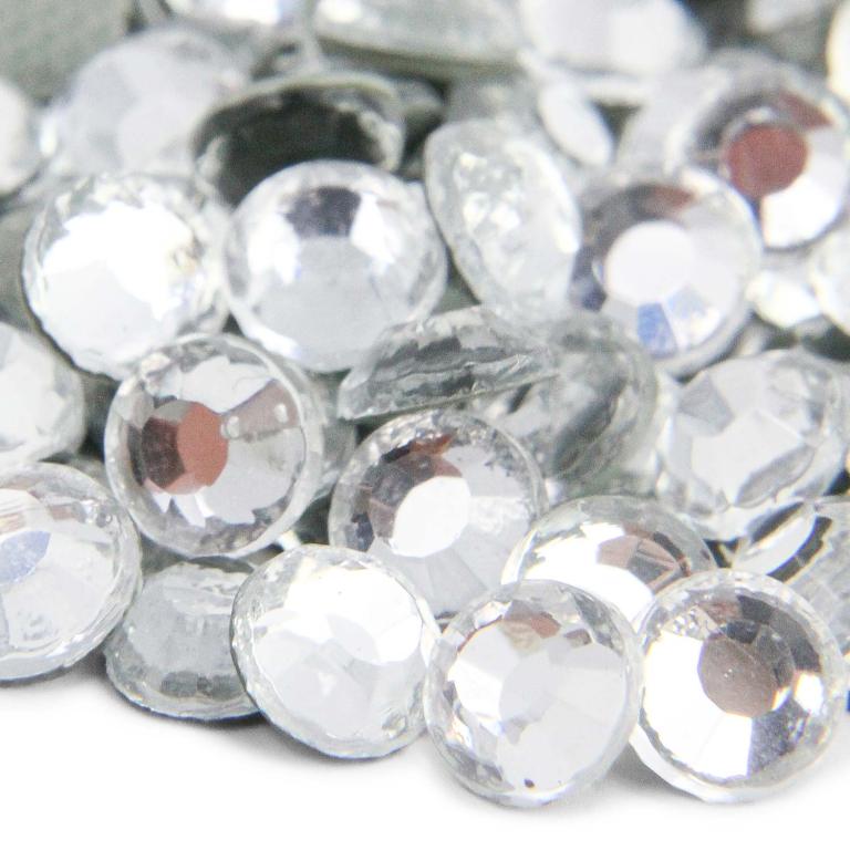Machine cut crystal rhinestones in clear round shape with faceted surfaces and gray glue backing reflecting light.