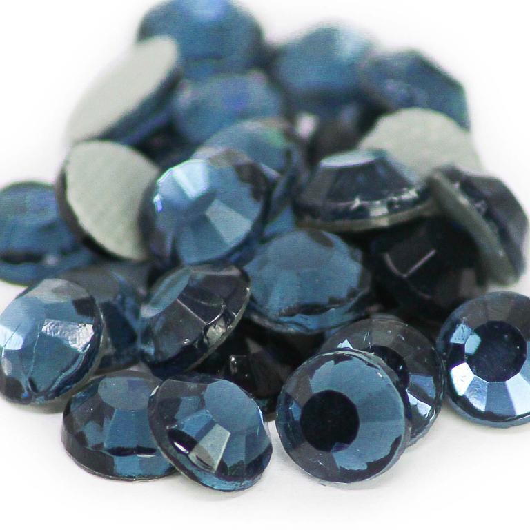 A pile of machine cut crystal rhinestones in dark teal faceted with gray glue backing and varying sizes.