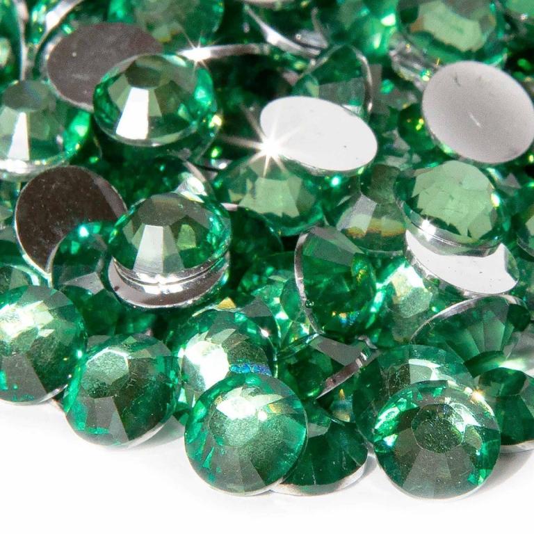 Emerald green resin stones with faceted surfaces and silver backing scattered on a white background reflecting light.