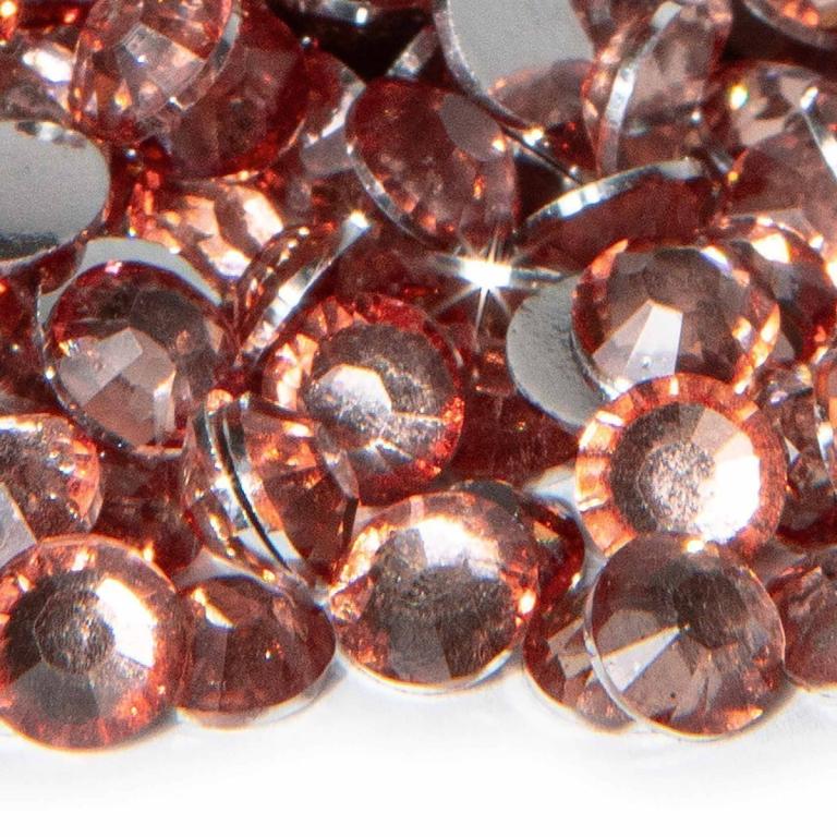 A pile of light rose resin stones with faceted surfaces and silver backing reflecting light and showing various sizes.