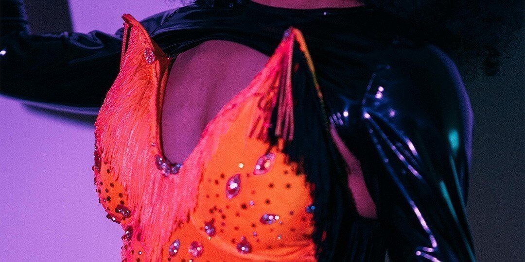 Close-up&amp;&#x23;x20&#x3B;of&amp;&#x23;x20&#x3B;drag&amp;&#x23;x20&#x3B;costume&amp;&#x23;x20&#x3B;with&amp;&#x23;x20&#x3B;orange&amp;&#x23;x20&#x3B;rhinestone&amp;&#x23;x20&#x3B;fringe&amp;&#x23;x20&#x3B;detail&amp;&#x23;x20&#x3B;under&amp;&#x23;x20&#x3B;stage&amp;&#x23;x20&#x3B;lighting