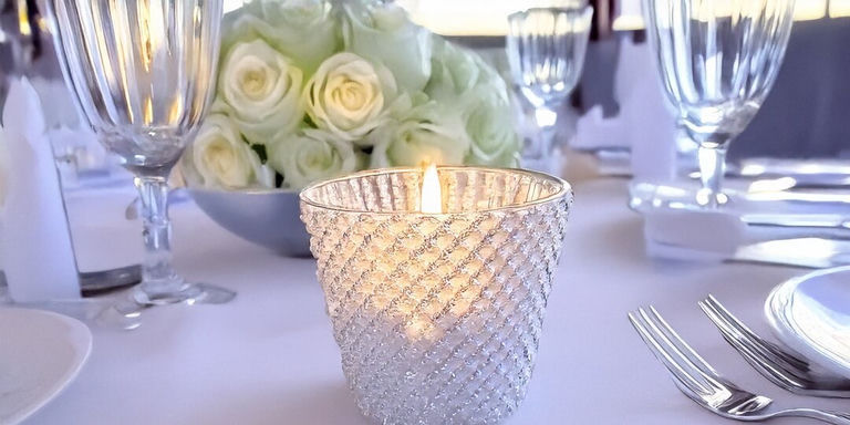 Portavelas de votiva cubiertos de pedrería con patrón de diamante brillando en una mesa de recepción de boda con centro de mesa de rosas blancas