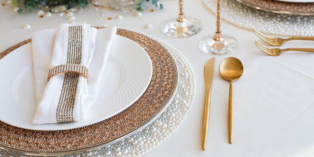 Mise&amp;&#x23;x20&#x3B;de&amp;&#x23;x20&#x3B;table&amp;&#x23;x20&#x3B;luxueuse&amp;&#x23;x20&#x3B;avec&amp;&#x23;x20&#x3B;assiette&amp;&#x23;x20&#x3B;plate&amp;&#x23;x20&#x3B;blanche&amp;&#x23;x20&#x3B;sur&amp;&#x23;x20&#x3B;assiette&amp;&#x23;x20&#x3B;de&amp;&#x23;x20&#x3B;pr&amp;&#x23;xE9&#x3B;sentation&amp;&#x23;x20&#x3B;en&amp;&#x23;x20&#x3B;strass&amp;&#x23;x20&#x3B;bronze,&amp;&#x23;x20&#x3B;superpos&amp;&#x23;xE9&#x3B;e&amp;&#x23;x20&#x3B;&amp;&#x23;xE0&#x3B;&amp;&#x23;x20&#x3B;un&amp;&#x23;x20&#x3B;set&amp;&#x23;x20&#x3B;de&amp;&#x23;x20&#x3B;table&amp;&#x23;x20&#x3B;blanc&amp;&#x23;x20&#x3B;&amp;&#x23;xE0&#x3B;&amp;&#x23;x20&#x3B;perles.&amp;&#x23;x20&#x3B;Serviette&amp;&#x23;x20&#x3B;blanche&amp;&#x23;x20&#x3B;maintenue&amp;&#x23;x20&#x3B;par&amp;&#x23;x20&#x3B;un&amp;&#x23;x20&#x3B;lien&amp;&#x23;x20&#x3B;dor&amp;&#x23;xE9&#x3B;&amp;&#x23;x20&#x3B;en&amp;&#x23;x20&#x3B;strass,&amp;&#x23;x20&#x3B;accompagn&amp;&#x23;xE9&#x3B;e&amp;&#x23;x20&#x3B;de&amp;&#x23;x20&#x3B;couverts&amp;&#x23;x20&#x3B;dor&amp;&#x23;xE9&#x3B;s&amp;&#x23;x20&#x3B;et&amp;&#x23;x20&#x3B;de&amp;&#x23;x20&#x3B;verres&amp;&#x23;x20&#x3B;en&amp;&#x23;x20&#x3B;cristal&amp;&#x23;x20&#x3B;sur&amp;&#x23;x20&#x3B;nappe&amp;&#x23;x20&#x3B;blanche,&amp;&#x23;x20&#x3B;avec&amp;&#x23;x20&#x3B;des&amp;&#x23;x20&#x3B;touches&amp;&#x23;x20&#x3B;de&amp;&#x23;x20&#x3B;verdure&amp;&#x23;x20&#x3B;en&amp;&#x23;x20&#x3B;arri&amp;&#x23;xE8&#x3B;re-plan.