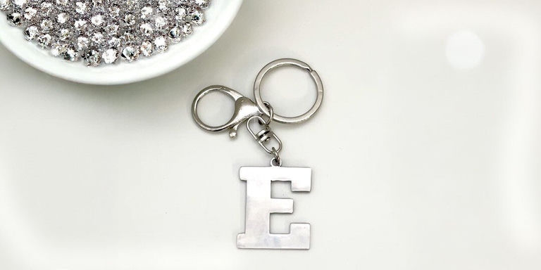 A metal keychain with letter E charm and rhinestones displayed on white surface
