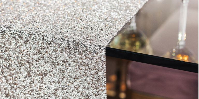 Una vista detallada en primer plano que muestra la textura intrincada de diamantes de plata. La superficie brillante captura y refleja la luz, creando un patrón glamoroso y texturizado. Una superficie reflectante oscura es parcialmente visible en el fondo desenfocado.
