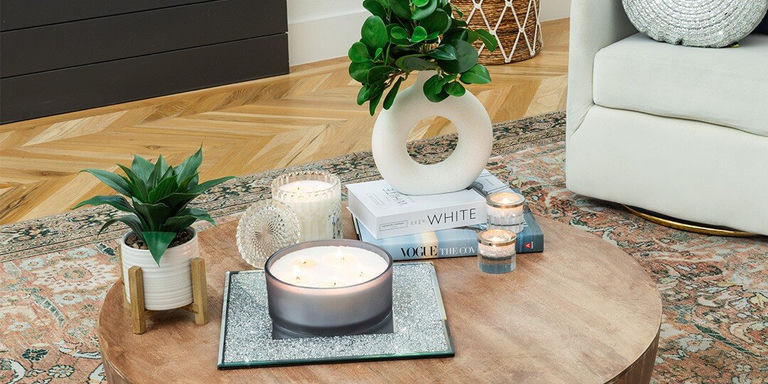 Round wooden coffee table styled with large candle on sparkly silver tray, stack of coffee table books including
