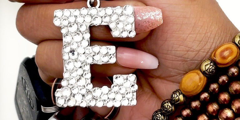 A hand wearing a decorative beaded bracelet holds up a finished letter