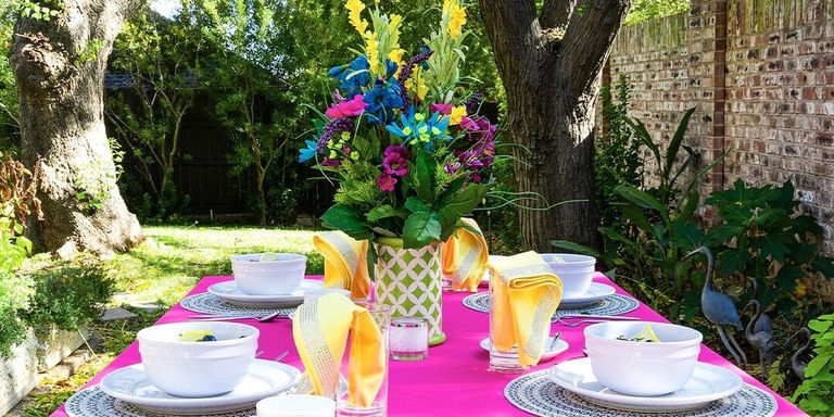 mesa de jardín exterior brillante con mantel rosa brillante, servilletas amarillas y centro floral colorido