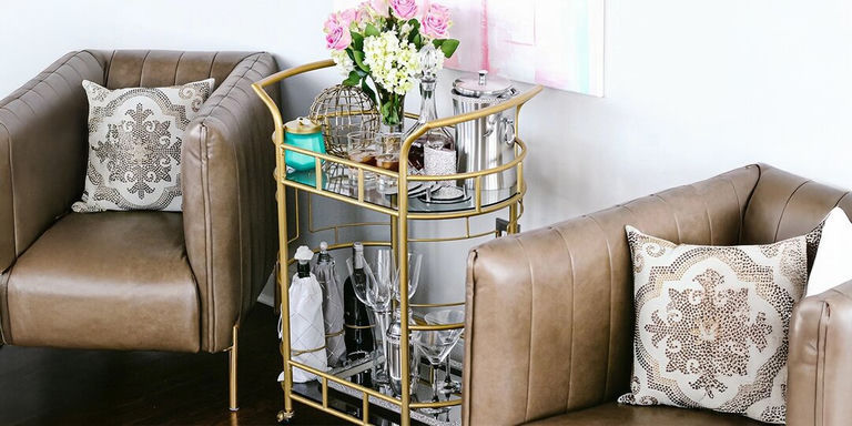 glam bar cart with gold frame, fresh flowers, and rhinestone pillows in leather chairs