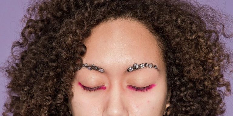 Primer plano de ojos cerrados con pedrerías acrílicas negras delineando las cejas sobre fondo morado