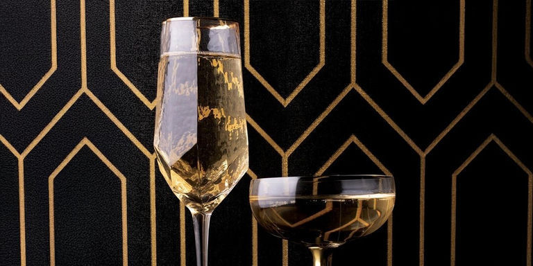 Flûte à champagne et verre coupe devant un motif de papier peint Art Déco noir et or