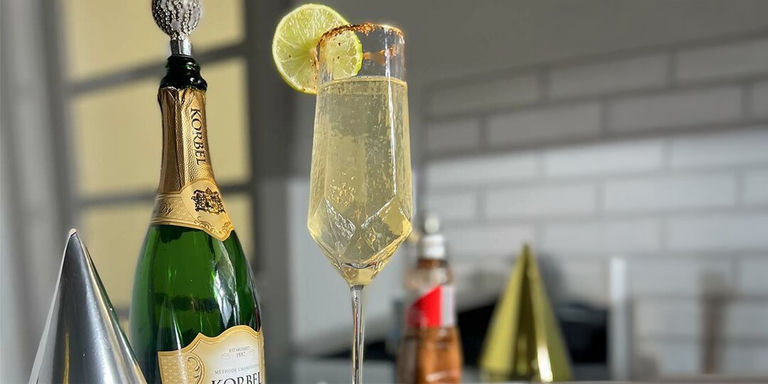 champagne margarita in rhinestone-stemmed flute with lime slice garnish beside Korbel bottle