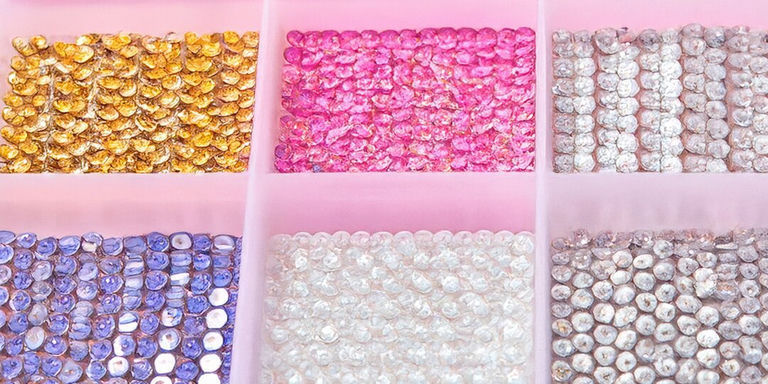 Plastic rhinestone storage box with compartments organized by color on pink background