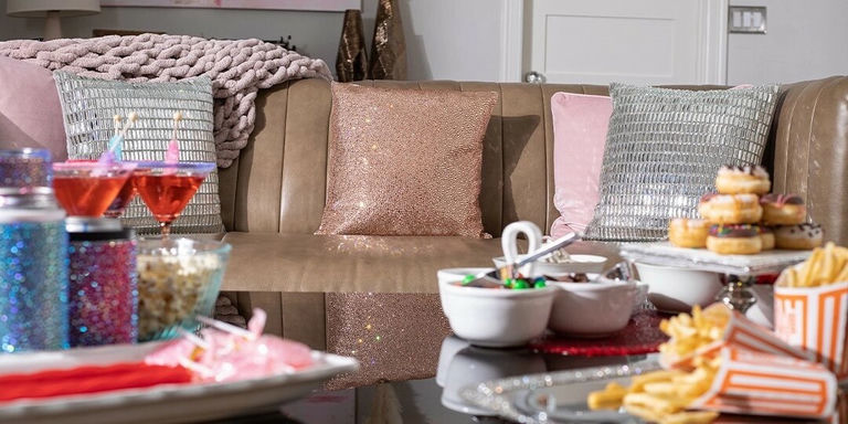 Configuración de sofá acogedora con almohadas glamorosas, acentos rosados y aperitivos para la noche de decoraciones de pedrería de Galentine