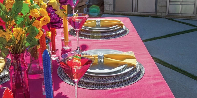 Mesa de comedor glamorosa al aire libre con mantel de terciopelo rosa, cargadores de pedrería y servilletas amarillas