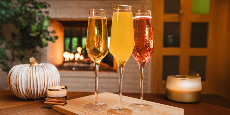 Trío de cócteles de mimosas de otoño en copas Prism con decoración otoñal en el fondo