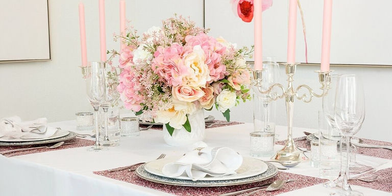 Centre de table floral rose et crème avec bougies effilées roses et décoration de table argentée