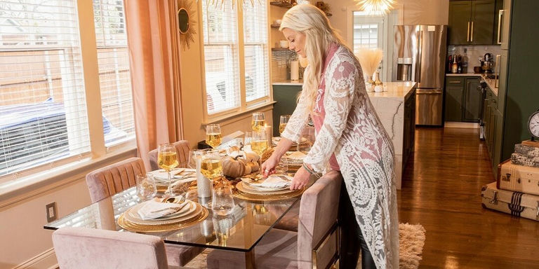 hôte préparant une table d’automne glamour avec des accents dorés et des chaises en velours