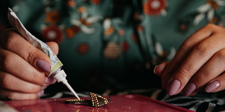 Hands applying rhinestones to jewelry with glue and tweezers