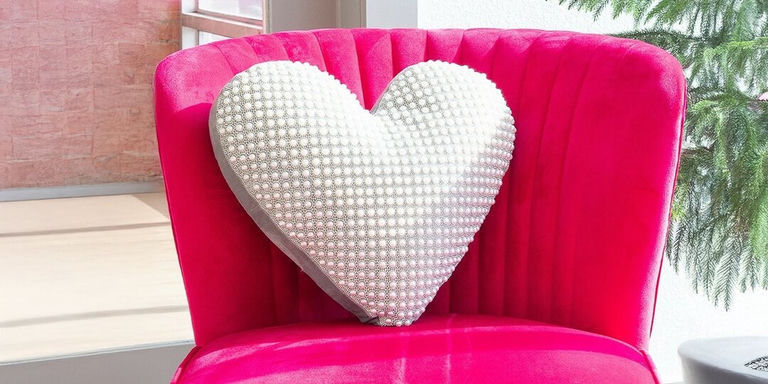 almohada en forma de corazón con pedrería blanca en una silla de terciopelo rosa intenso