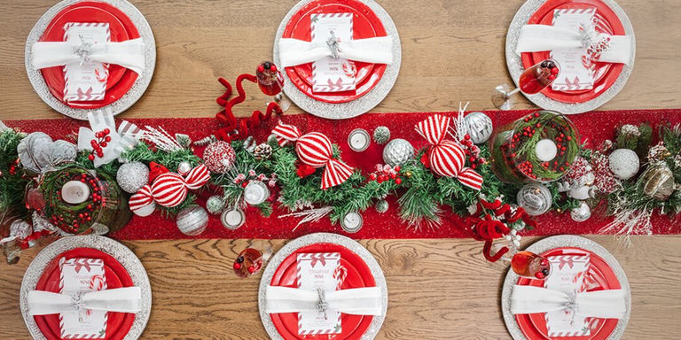 overhead view of holiday table set with red plates, rhinestone chargers, and peppermint garland