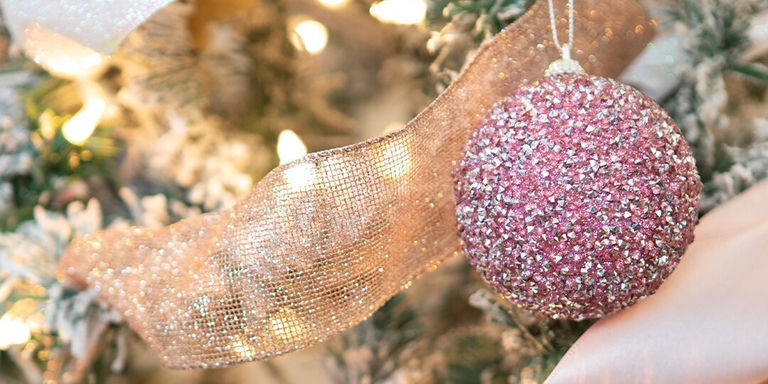 close-up of pink rhinestone Christmas ornament on lit and frosted tree with gold ribbon