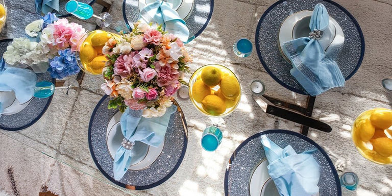 Decoración de mesa de Día de la Madre glamorosa con florales rosados y blancos, platos de carga de pedrería y servilletas azules suaves