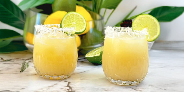 margaritas à la noix de coco jaunes avec bords de verre en noix de coco râpée et garniture de citron vert sur comptoir en marbre